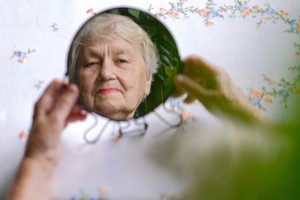 Ältere Frau betrachtet sich im Spiegel